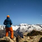 A lone climber stands on a rocky peak under a starlit sky in Cerler, Spain, during winter.